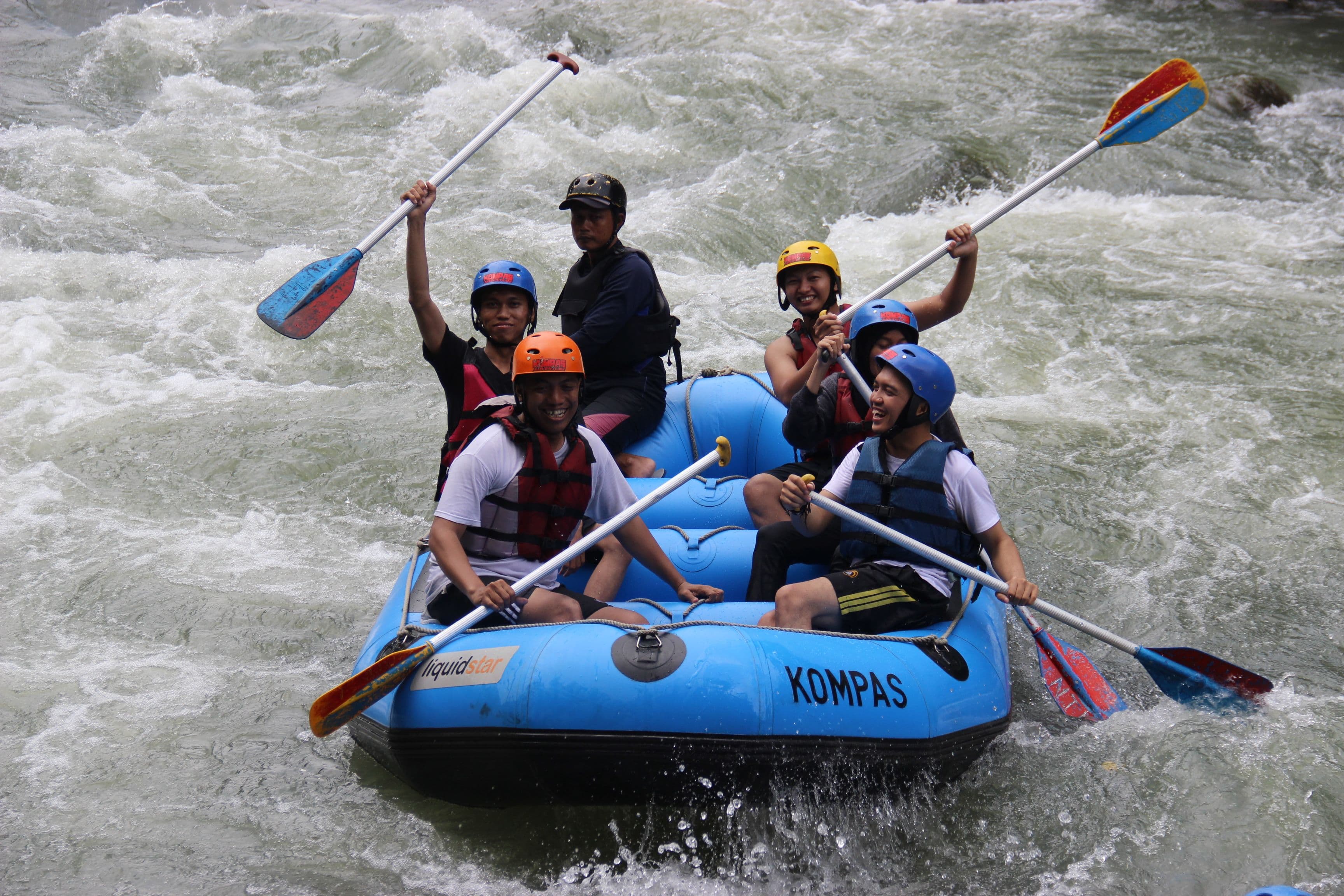 Group whitewater rafting together, paddles raised in celebration
