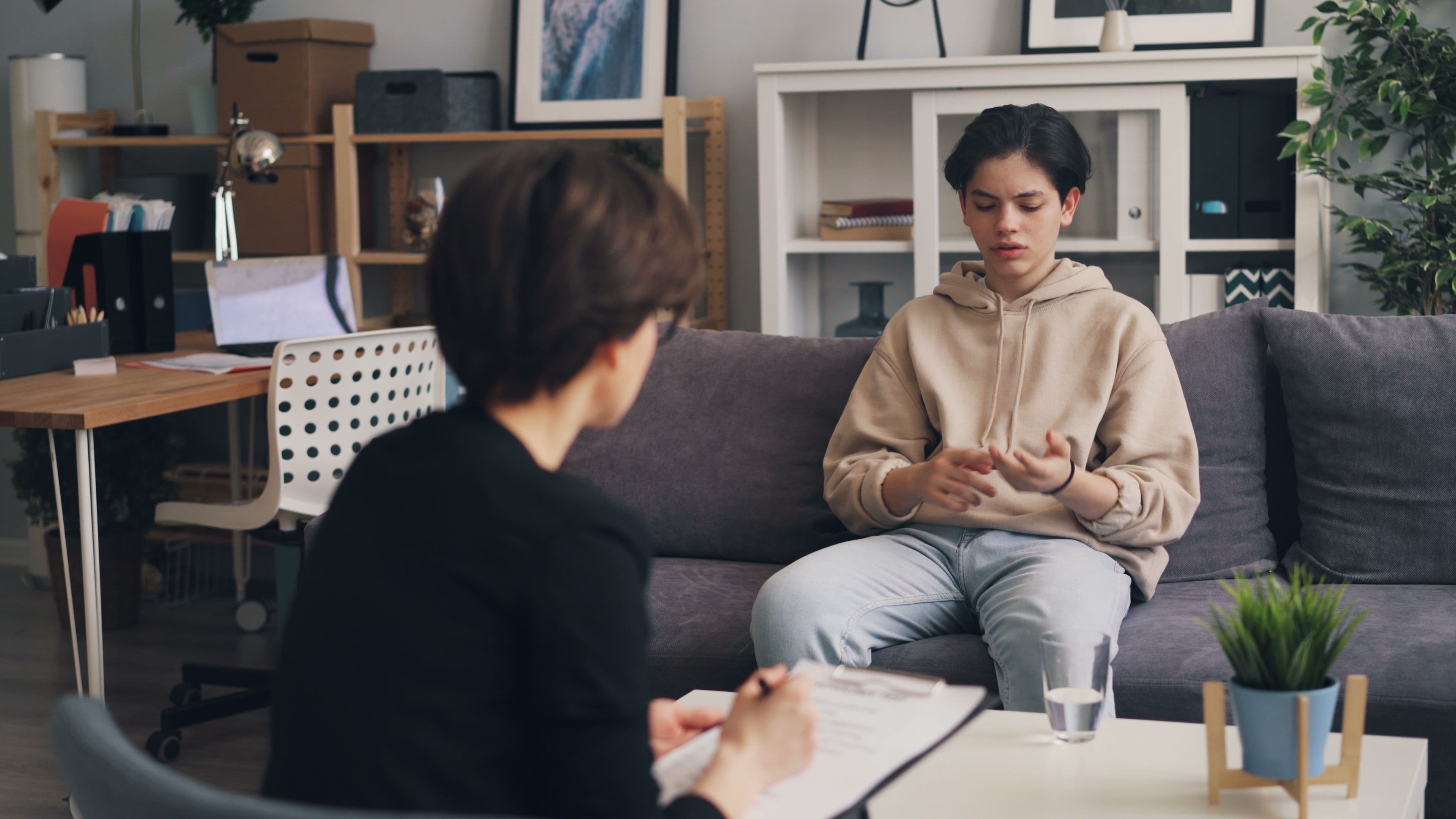 Teen in a hoodie talking with a therapist who is taking notes