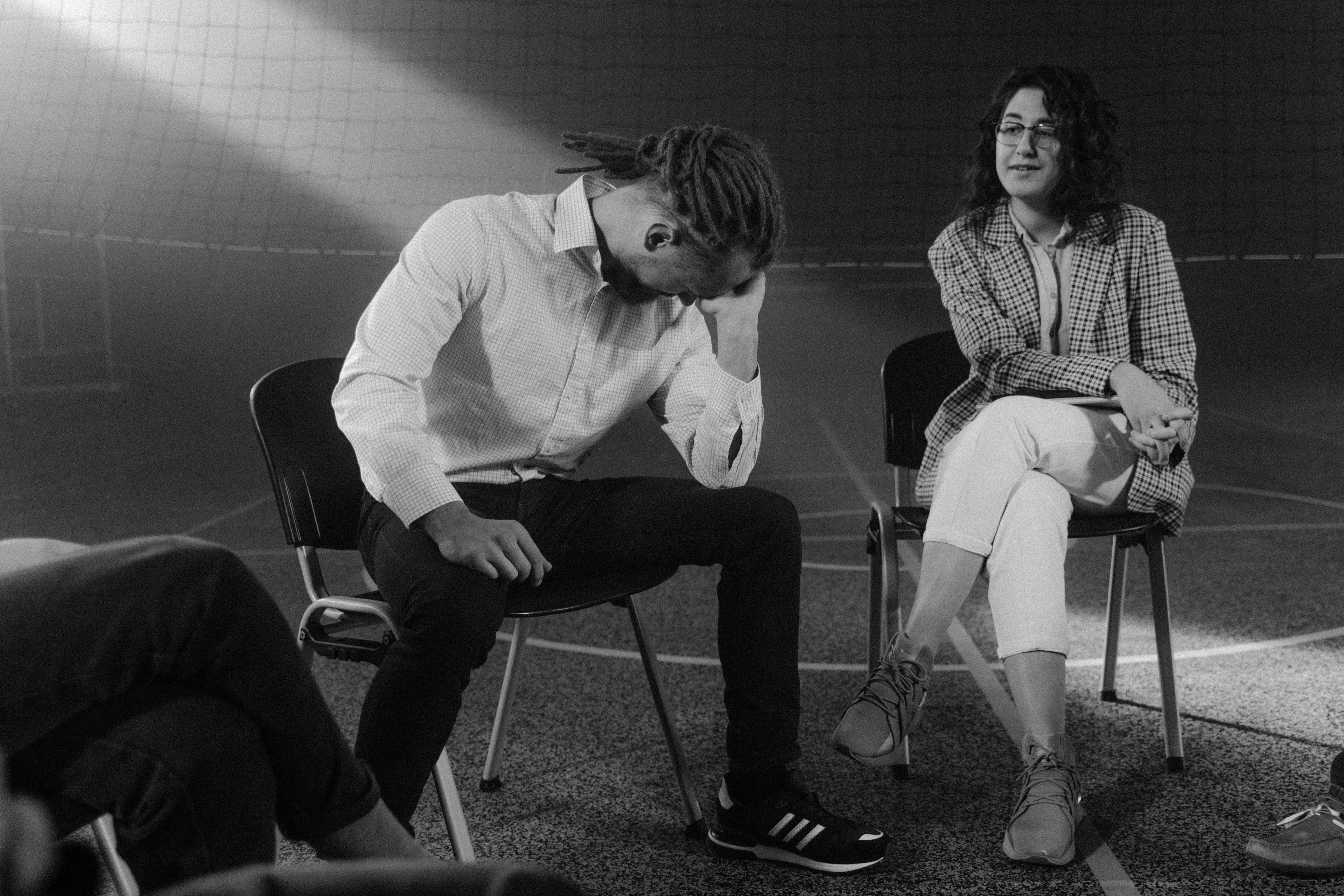 Black-and-white photo of a support group sitting in a circle, one man holding his head