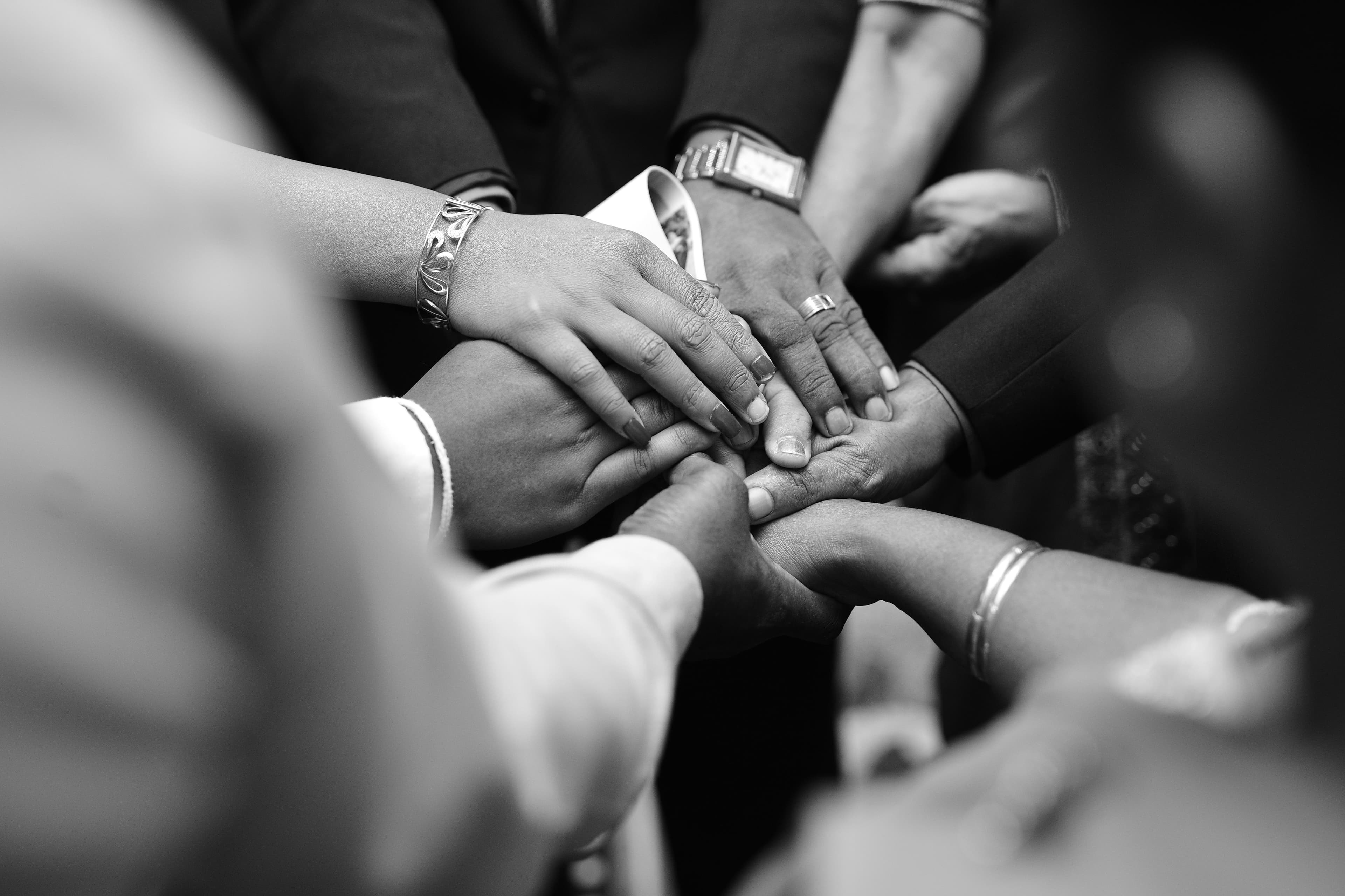 Black-and-white close-up of many hands stacked together