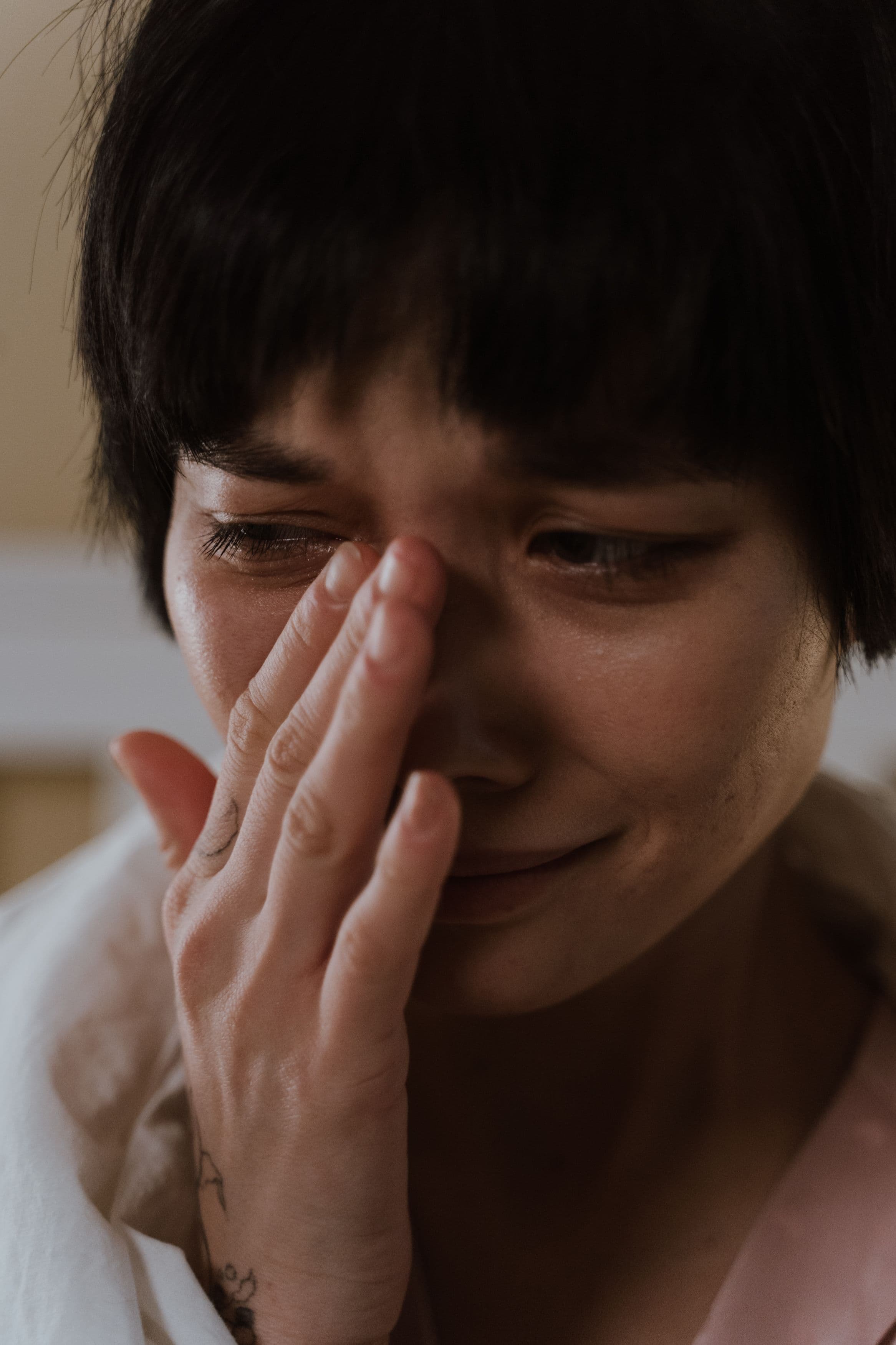 A woman with short dark hair cries quietly, wiping a tear from her eye with her hand.